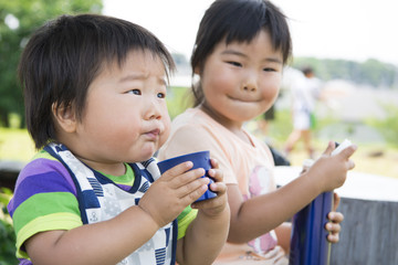 公園で水筒のお茶を飲む姉弟