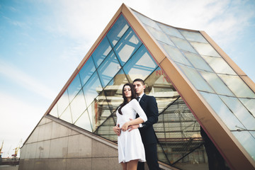 Stylish loving couple kissing and hugging near modern building