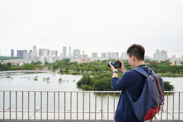 Rear view of Vietnamese guy taking photo of city across the river