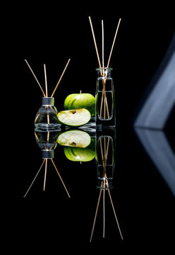 Air fresheners with green apple scent in a beautiful glass jars with sticks and whole green apple and a slice of apple with reflection isolated on a black background
