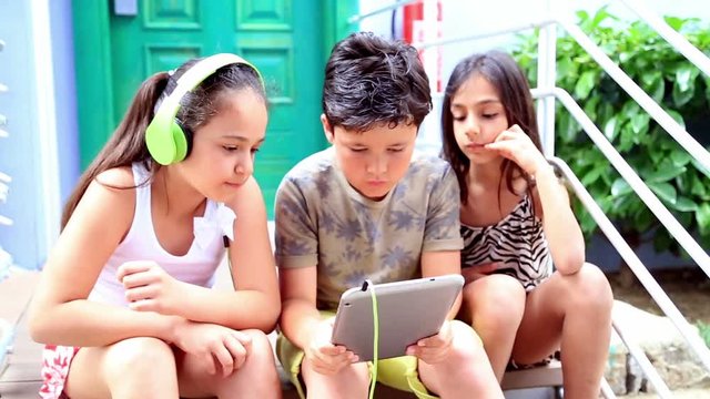 Close up portrait of three caucasian young girls and boy playing together on digital tablet