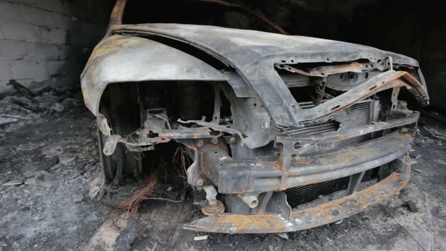pan footage of burned out car in garage after fire, grunge apocaliptic scene