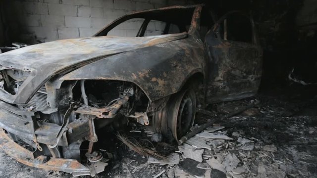 pan footage of burned out car in garage after fire, grunge apocaliptic scene