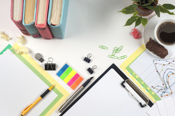 Office table desk with set of colorful supplies, white blank note pad, cup, pen, crumpled paper, flower on white background. Top view and copy space for text