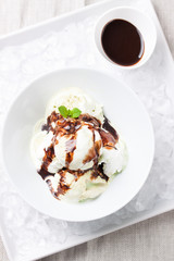 Vanilla and pistachio ice cream with chocolate sauce in a bowl on a plate with ice, top view