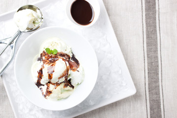 Vanilla and pistachio ice cream with chocolate sauce in a bowl on a plate with ice, top view