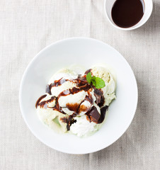 Vanilla and pistachio ice cream with chocolate sauce in a bowl on a plate on a linen textile, top view