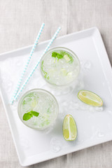 Non alcohol cold mojito cocktail with fresh lime, mint and crushed ice on plate with ice a linen textile, top view