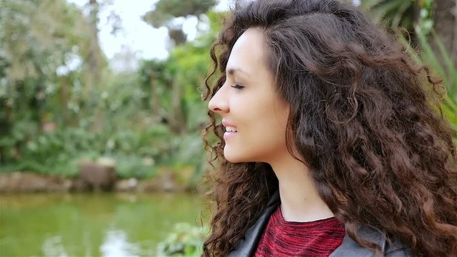 Portrait of a happy young woman with beautiful curly hair smiling in a park, slow motion