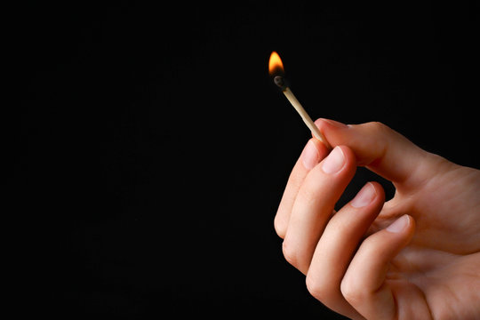 girl holding burning match in hand on black wooden background