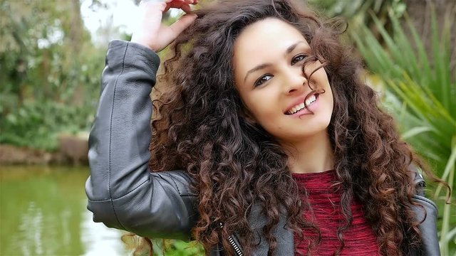 Portrait of a happy young woman with beautiful curly hair smiling in a park, slow motion