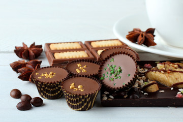candies and chocolates with cinnamon and anise with coffee beans on white wooden background with Cup of strong coffee