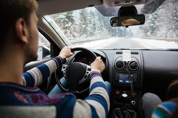 Handsome young driver driving through winter forest