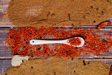 White spoon with saffron near different colorful spices on wooden background.  Various spices selection. Closeup.