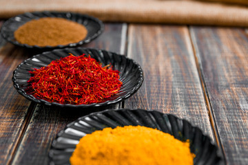Spices in black ceramic plates on wooden background. Various spices selection, closeup. Saffron, turmeric, curry