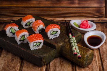 Sushi Rolls with salmon and cucumber served on wooden board with soy sause and ginger shape rose  on wooden  background. Selective focus