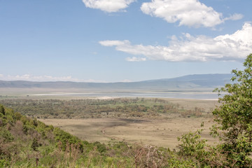 View on huge Ngorongoro caldera (extinct volcano crater) with large lake from cleft against blue sky background. Great Rift Valley, Tanzania, East Africa.

