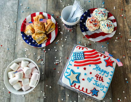 4th of July Kuchen mit Marshmallows, Cupcakes und Hot Dogs auf Holztisch von oben gesehen