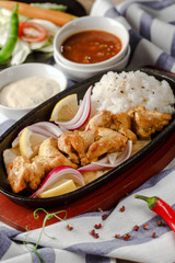 Skewers of grilled chicken in a pan with a side dish of rice