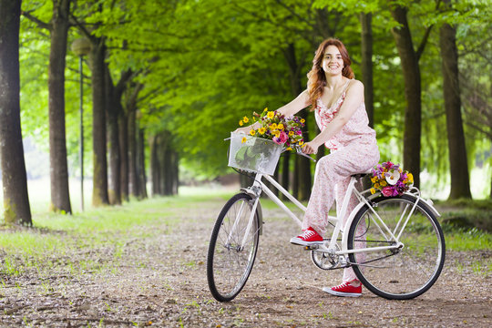 Beautiful young woman standing with a vintage bicycle at the par