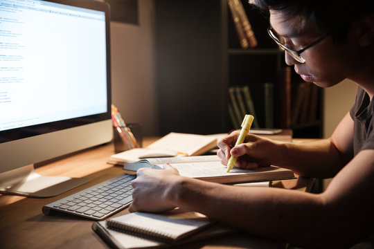 Serious Man Studying With Books And Computer In Dark Room