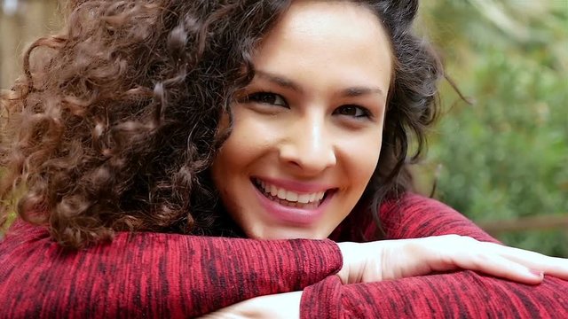 Portrait of happy young woman with beautiful curly hair leaning head on her arms, slow motion
