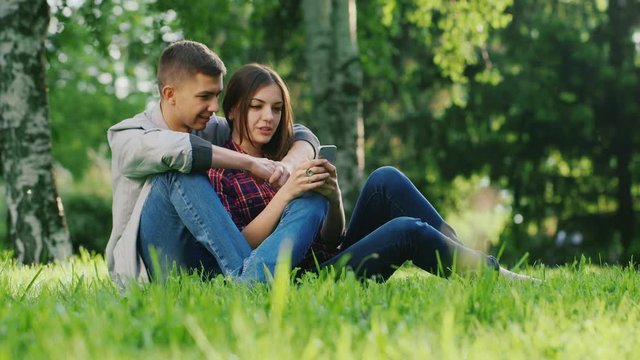 An attractive couple sitting on the grass in the park, use the phone, hugging