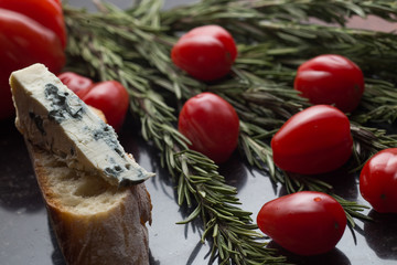 Blue cheese with french baguette, tomato and herbs on black marble table. Traditional snacks in France and Italy.