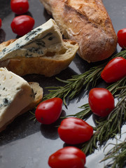 Blue cheese with french baguette, tomato and herbs on black marble table. Traditional snacks in France and Italy.