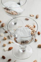 Granola with yoghurt, nuts and fruits in glass bowl on light background. Delicious, healthy sweet dessert for breakfast. Cereal, muesli.  Copy space, closeup.