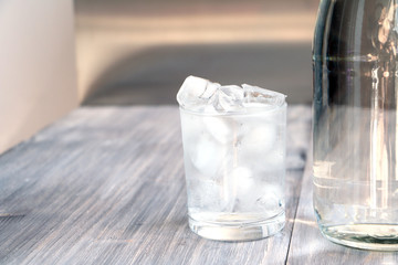 Fresh pure water with ice cubes in a glass and bottle on a wooden table.