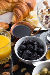 Breakfast assorted yoghurt, granola, coffee, juice, croissant, olives. Appetizer mix with morning dishes. Healthy, fresh, delicious food on dark background. Top view. Copy space.