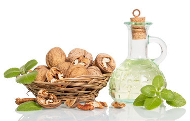 Wicker bowl with walnuts and oil bottle isolated on white.