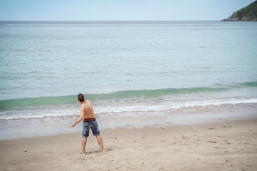 Fototapeta na wymiar Man plays throwing rocks at the beach on vacation