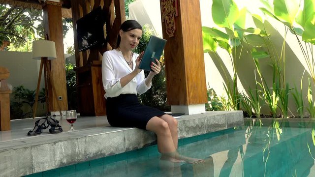 Young businesswoman working one tablet computer and drinking wine sitting by the swimming pool, 4K
