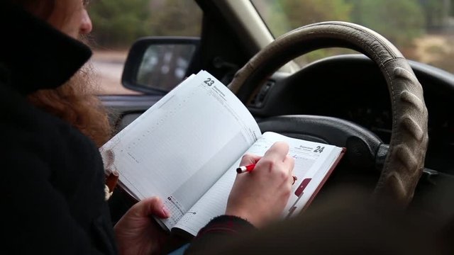 Woman in the car makes an entry in the notebook