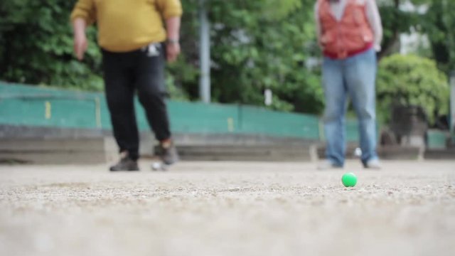 Seniors Playing Petanque In The Park. Pétanque is a form of boules where the goal is to throw steel balls as close as possible to a small wooden ball called a cochonnet.