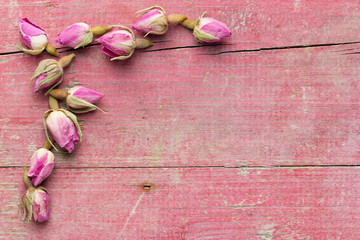 Lateral border of pink dried roses on wooden pink background. Top view with copy space. Sweet rustic card.