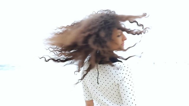 Young woman shaking her beautiful curly hair on white background, slow motion