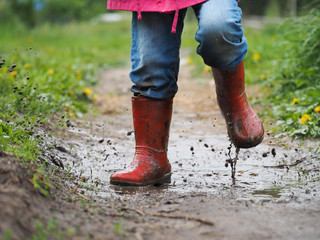 child's feet in the muddy, wet jeans and rubber boots. The child jumps in a puddle 