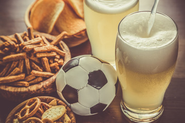 Pouring beer into glass with snacks and football