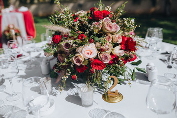 Wedding. Banquet. Grain. Artwork. At the banquet table with tablecloth colors Marsala, is the composition of flowers and greenery, cutlery and candles