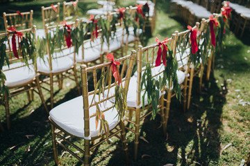 Wedding. Ceremony. Grain. Artwork. Chairs gold color stand on the lawn in the area of the wedding ceremony. On chairs decoration of greenery and tissue tapes
