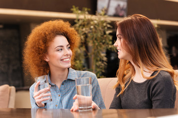 Two happy attractive young women drinking water in cafe
