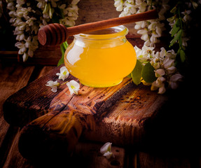 Sweet acacia honey in jars and acacia flowers on vintage wooden background. Toned image. Selective focus. Square image.