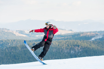 Male snowboarder riding on his snowboard and taking his for the edge on top of a mountain against...