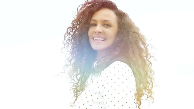 Portrait of happy young woman with beautiful curly hair on white background, sunshine effect, slow motion