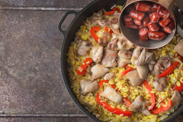 Adding smoked  sausages on the pan with cooking paella top view