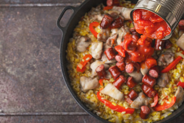 Adding chopped tomatoes on the pan with cooking paella top view