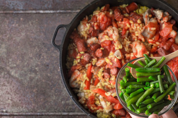 Adding French bean on the pan with cooking paella top view